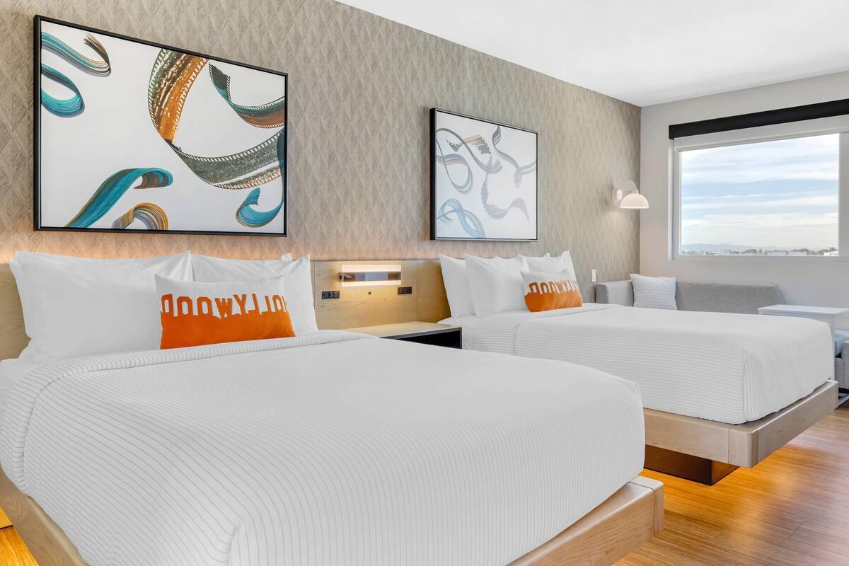 A hotel room with two beds, a large window, and abstract artwork on the walls.
