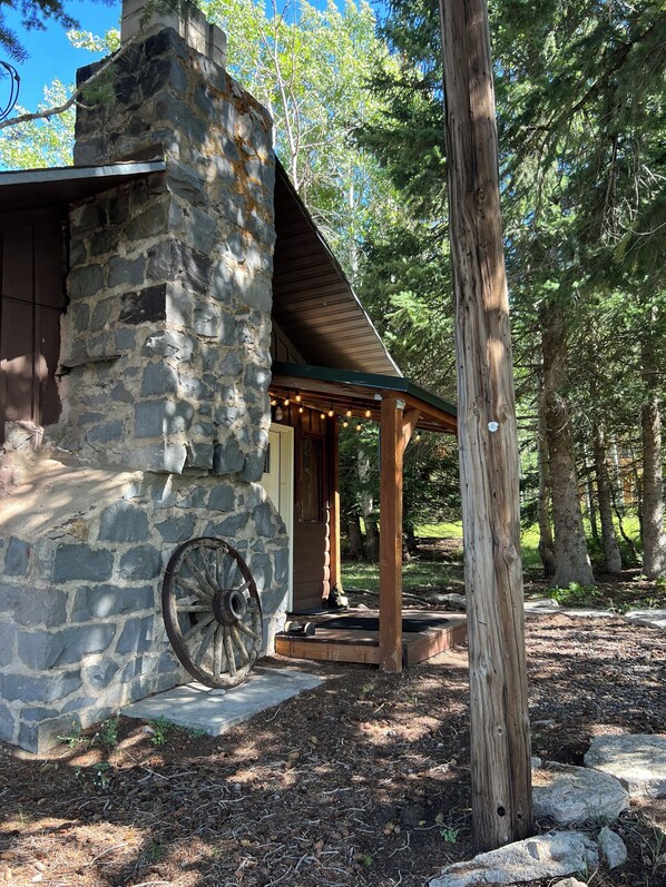 A rustic stone building with a wooden porch and a wheel.