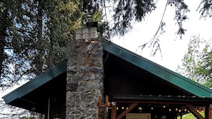 Eine rustikale Holzhütte mit einem Steinkamin, einer Holzterrasse und einem Schubkarren.