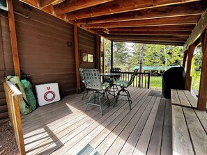 A wooden deck with a table and chairs, a grill, and a covered area with a window.