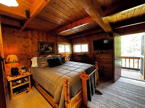 A wooden cabin bedroom with a bed, dresser, television, and windows.