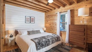 Een slaapkamer met houten lambrisering, een bed, nachtlampen, een dressoir en een raam met gordijnen.