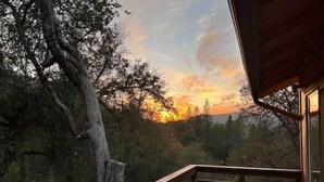 Puinen terassi, jossa on kaide, ja jolta avautuu näkymä metsäiseen maisemaan auringonlaskun aikaan.