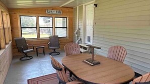 A covered outdoor dining area with a wooden table and chairs, a rug, and a sign that reads "SUN AND FUN". - Harlan County Lake Retreat (Republican City)