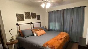 A bedroom with a bed, a ceiling fan, a nightstand, and a window with curtains. - Harlan County Lake Retreat (Republican City)