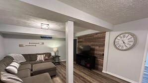 A modern living room with a sectional sofa, a flat-screen TV, and a wooden accent wall. - Harlan County Lake Retreat (Republican City)