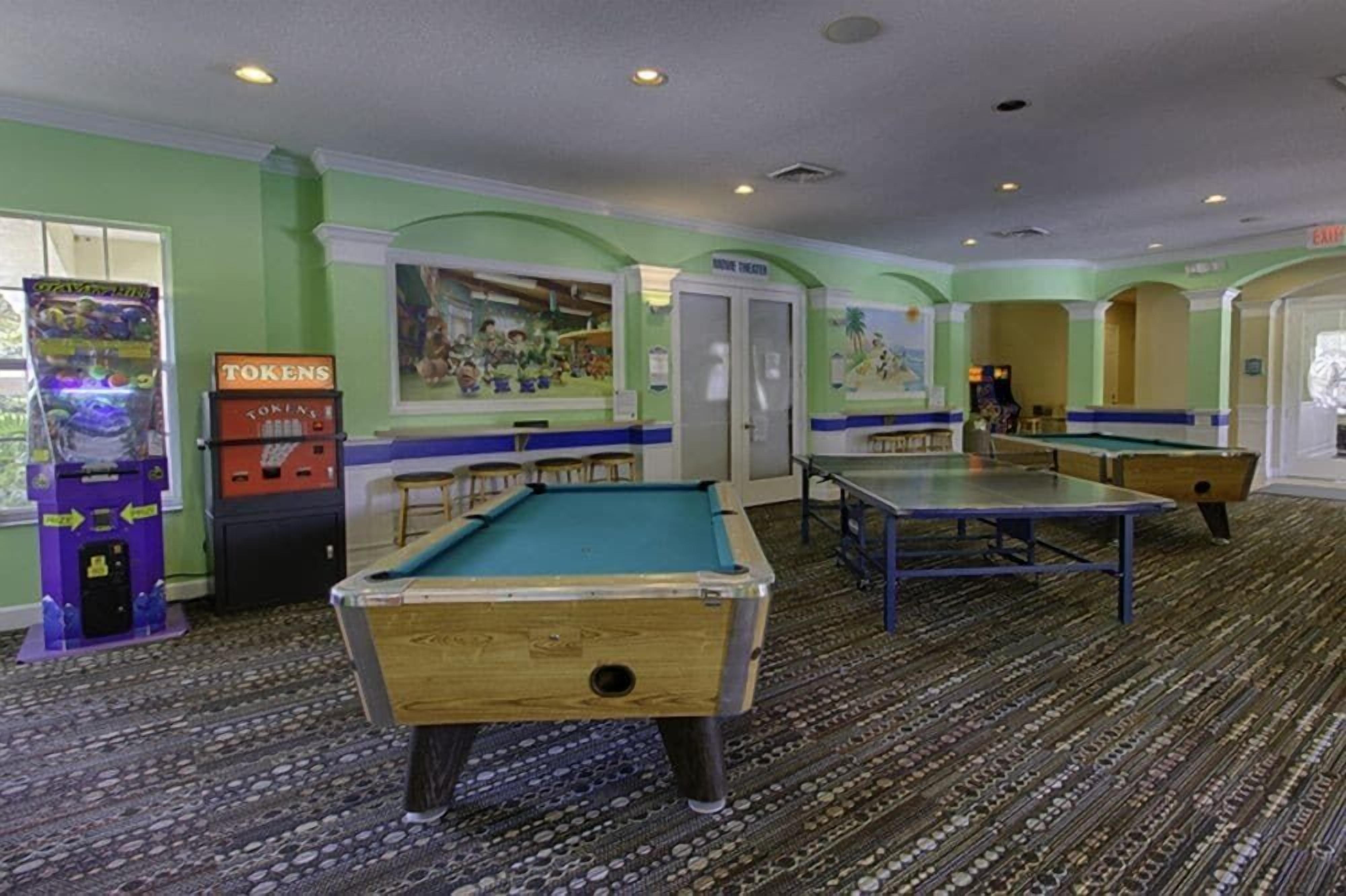 A pool table, a billiards table, and a foosball table in a room with green walls and patterned carpet.