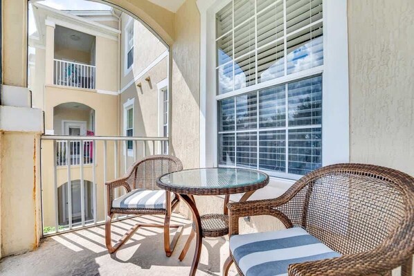 A balcony with wicker furniture, a glass table, and a view of the building's interior. - Epic Windsor Palms Parkside Retreat (Kissimmee)