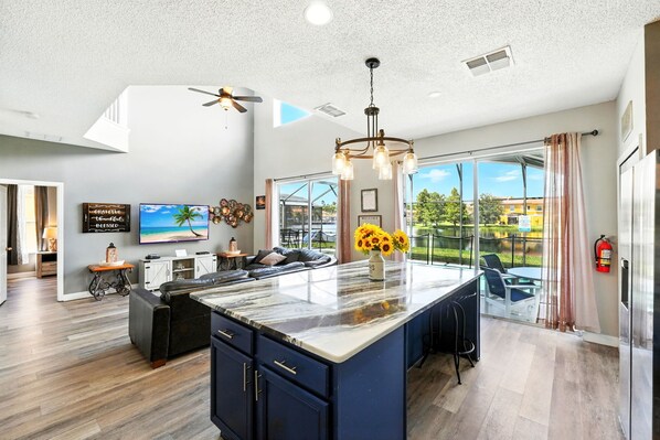 A modern kitchen with a large island, a dining area with a view, and a living room with a sofa and TV. - Wonderful Terra Verde Orlando Vacation Home (Kissimmee)