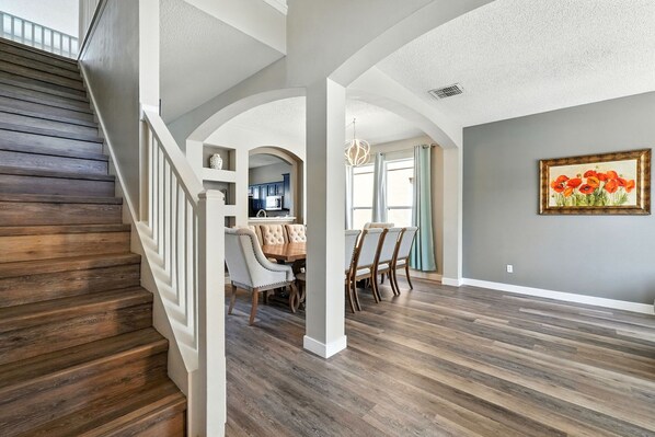 A spacious living area with a wooden staircase, a dining area with a wooden table and chairs, and a kitchen in the background. - Wonderful Terra Verde Orlando Vacation Home (Kissimmee)