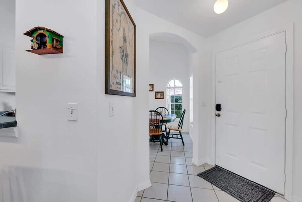 Un pasillo con una puerta blanca, un cuadro en la pared y un pequeño estante con una casita de juguete.