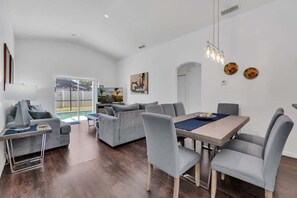 Una sala de estar moderna con comedor, sofás grises, una mesa de comedor de madera y vista a una piscina.