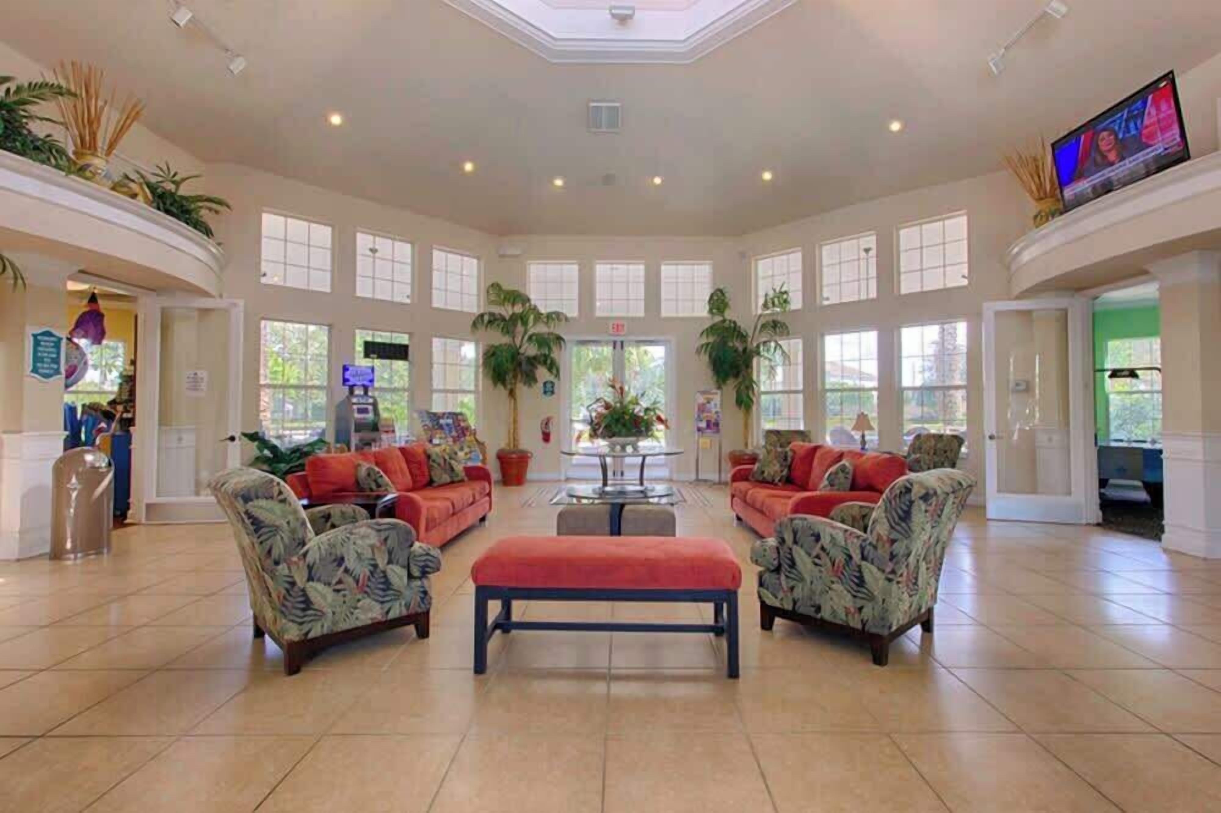A spacious lobby with a high ceiling, large windows, and a central seating area with a coffee table.