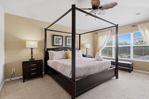 A four-poster bed with a ceiling fan, bedside tables, and a window with curtains.