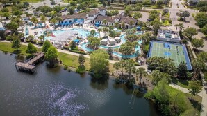 An aerial view of a resort with a central pool, tennis courts, and a dock over water. - Newly Completed Avatar 6 Bedroom Getaway (Kissimmee)