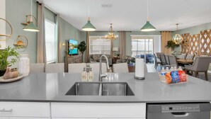 A modern kitchen with a central island, stainless steel sink, and overhead pendant lighting.