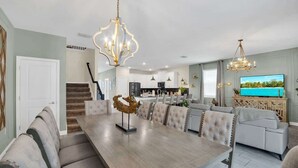 A spacious living room with a large dining table, comfortable seating, and a television.