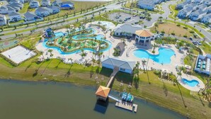 An aerial view of a resort with multiple swimming pools, a water slide, and a dock.