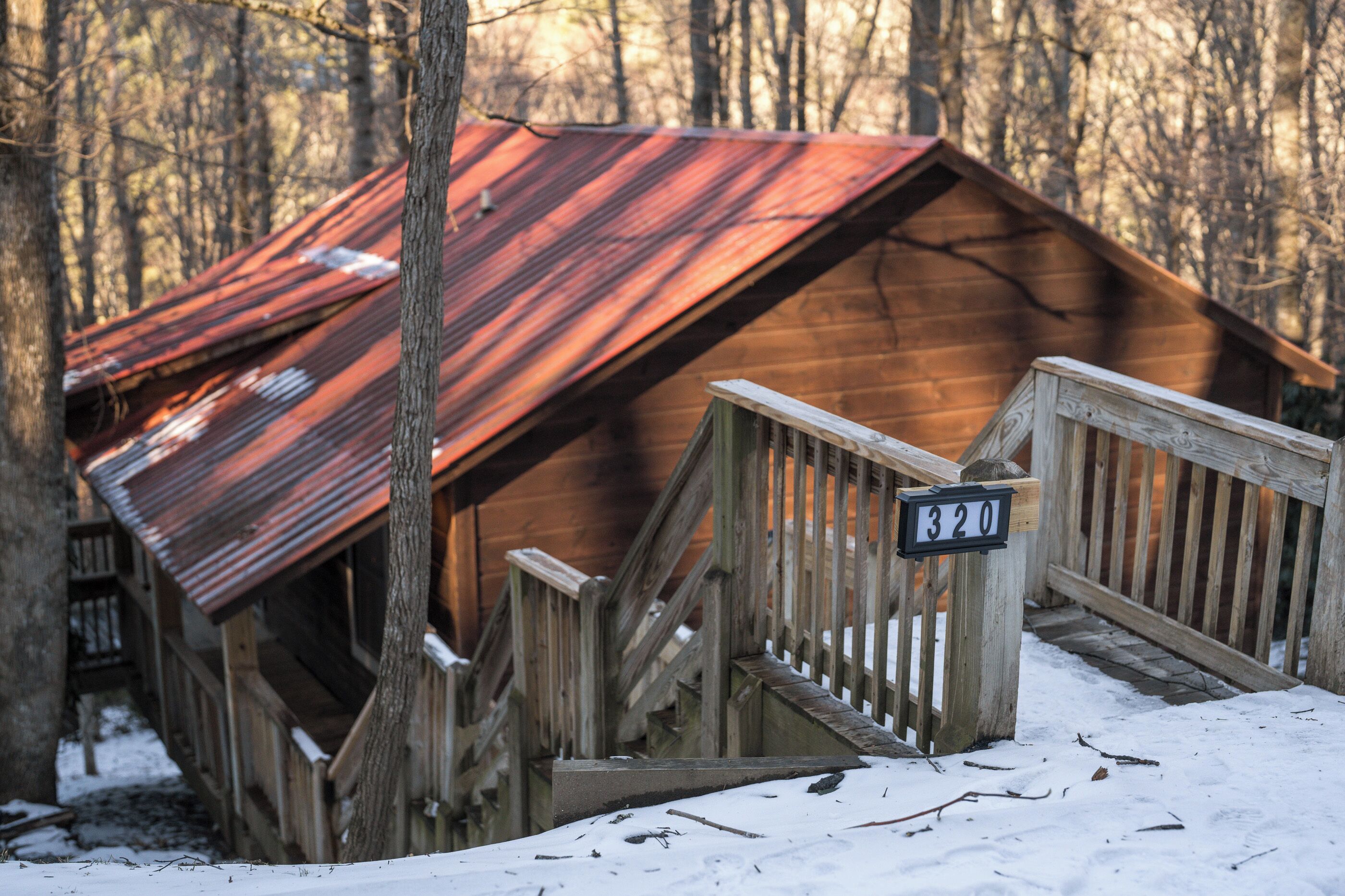 A rustic cabin with a metal roof, wooden staircase, and a number sign indicating its location.