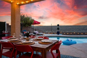 Un espace extérieur aménagé pour les repas, avec une piscine, des chaises rouges et une table dressée pour un repas.