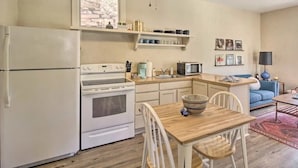 A compact kitchen with white appliances, a wooden dining table, and a blue sofa in the adjacent living area.