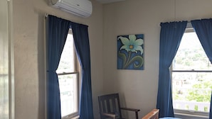 A bedroom with a bed, a wooden chair, a small table, a heater, and a ceiling fan.