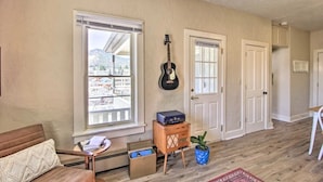 A living room with a large window, a guitar, a couch, a small table, and a potted plant.