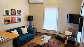 A compact living room with a blue sofa, a wooden coffee table, a patterned rug, a TV, and a small side table with a lamp.