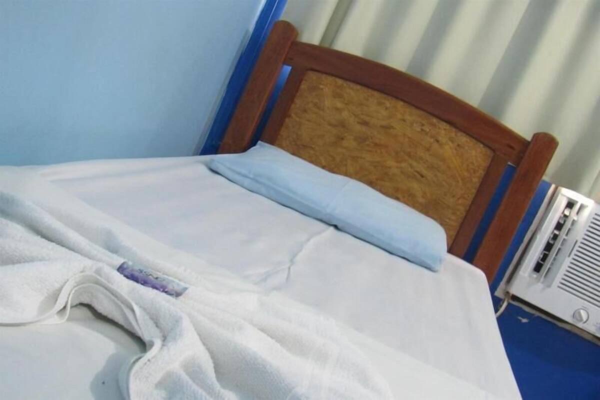 A bed with a wooden headboard, a white blanket, and a pillow.