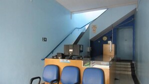 Zona de recepción con mostrador, sillas azules y una escalera que conduce a un piso superior.