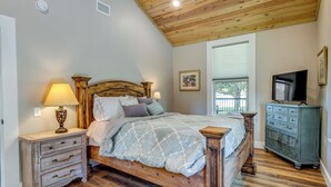 Een slaapkamer met een houten bed, een nachtkastje met een lamp, een dressoir en een televisie op een meubel.