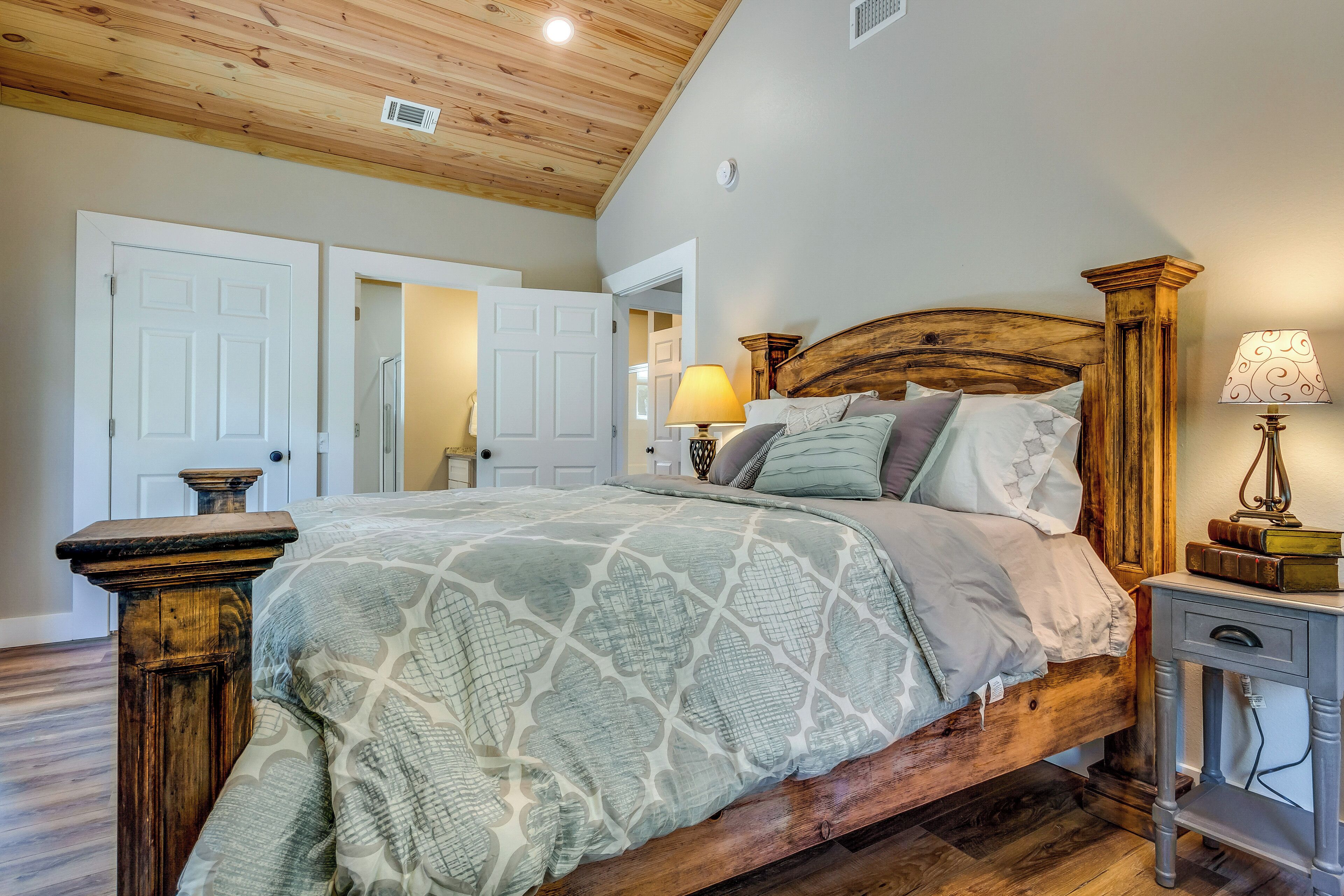 A bedroom with a wooden bed, a nightstand with a lamp, and a door leading to another room.