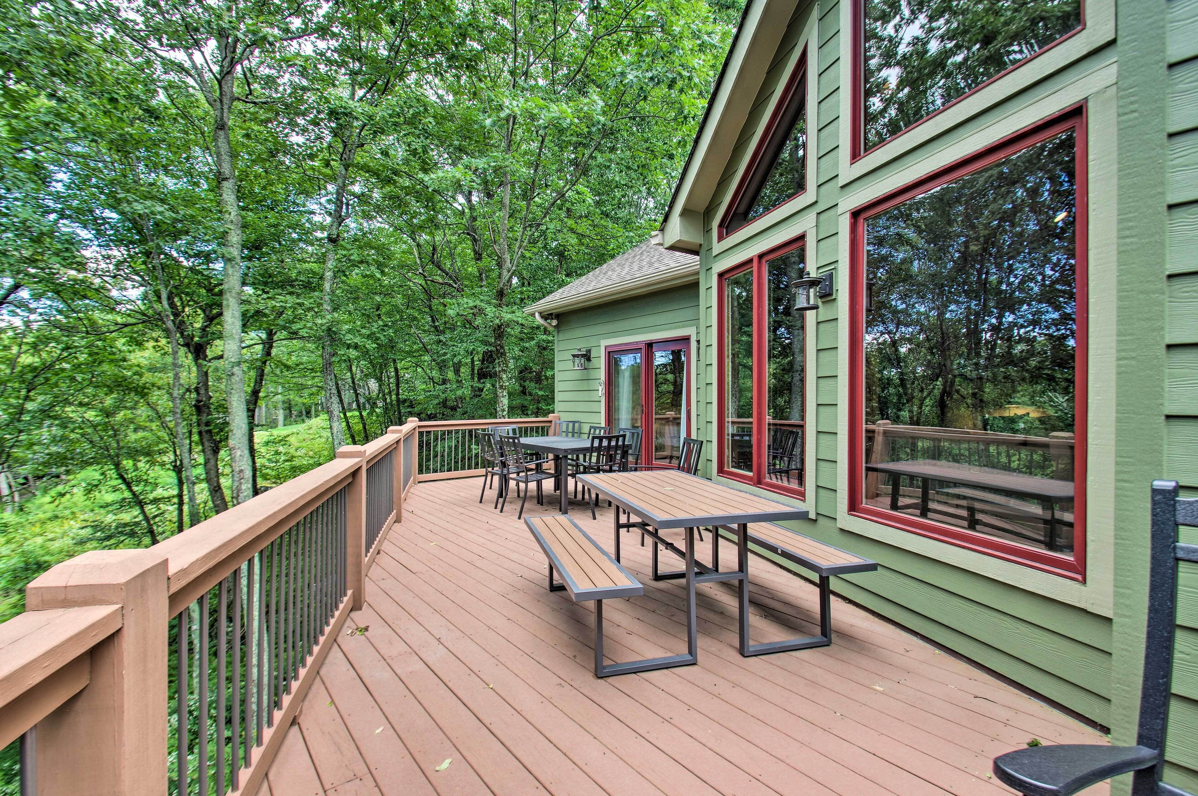 A wooden deck with picnic tables and chairs, surrounded by lush greenery.