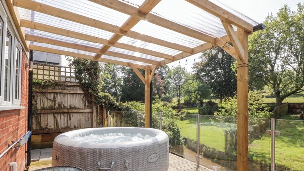 Un bain à remous sous une pergola en bois, avec une table en verre à proximité.