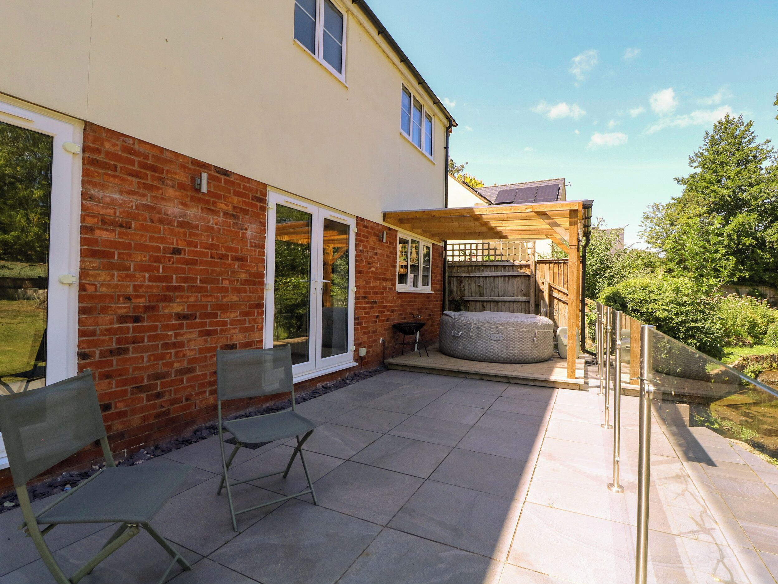 A patio area with a brick wall, a sliding glass door, a wooden pergola, and a large wicker sofa.