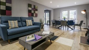 Un salon moderne avec un canapé bleu, une table basse sur laquelle sont posés des livres et une télécommande, et un coin repas avec des chaises et une table.