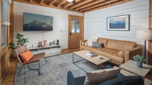 A cozy living room with a brown leather sofa, a blue armchair, a coffee table, and a TV mounted on the wall.