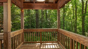 A wooden deck with a railing, surrounded by a forest.
