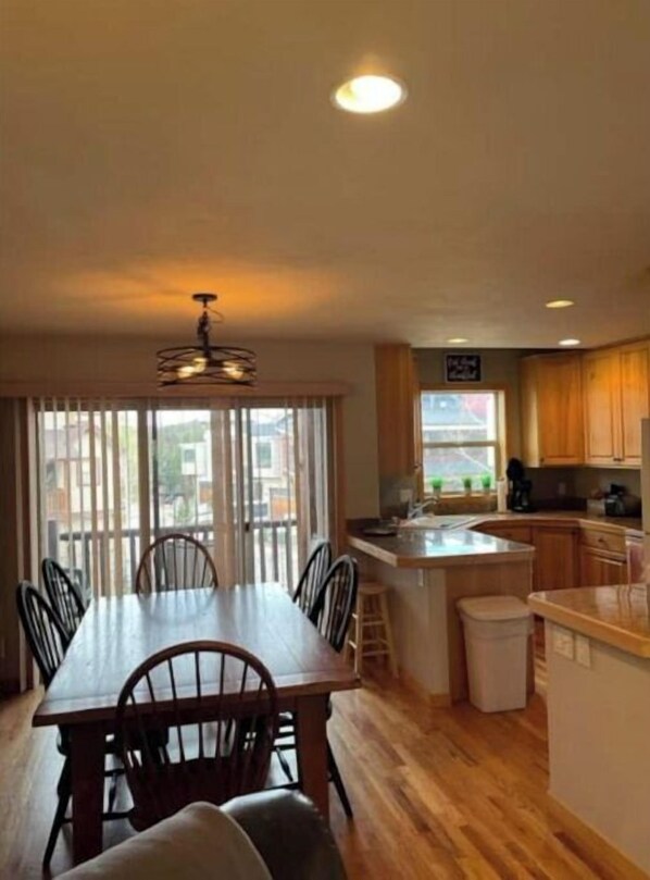 Enjoy meals in this dining area with a long table and chairs, adjacent to a kitchen with a sink and wooden cabinets.