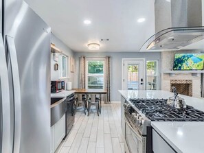 A modern kitchen with a stainless steel refrigerator, a gas stove, and a dining area with a table and chairs.