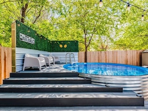 Un jardin avec un jacuzzi, des marches menant Ă un porche et un panneau accueillant les visiteurs.