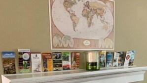 Une cheminée surmontée d’une étagère où sont exposés des livres et une carte du monde.