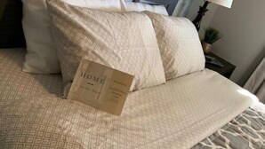 Un lit bien fait, avec une couvre-lit à motifs et des oreillers, une œuvre d’art encadrée au-dessus du lit, et une lampe sur une table de chevet.