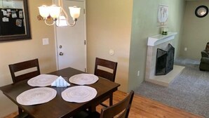 Un coin repas avec une table en bois foncé, quatre chaises et trois sets de table. Un lustre est suspendu au-dessus de la table.