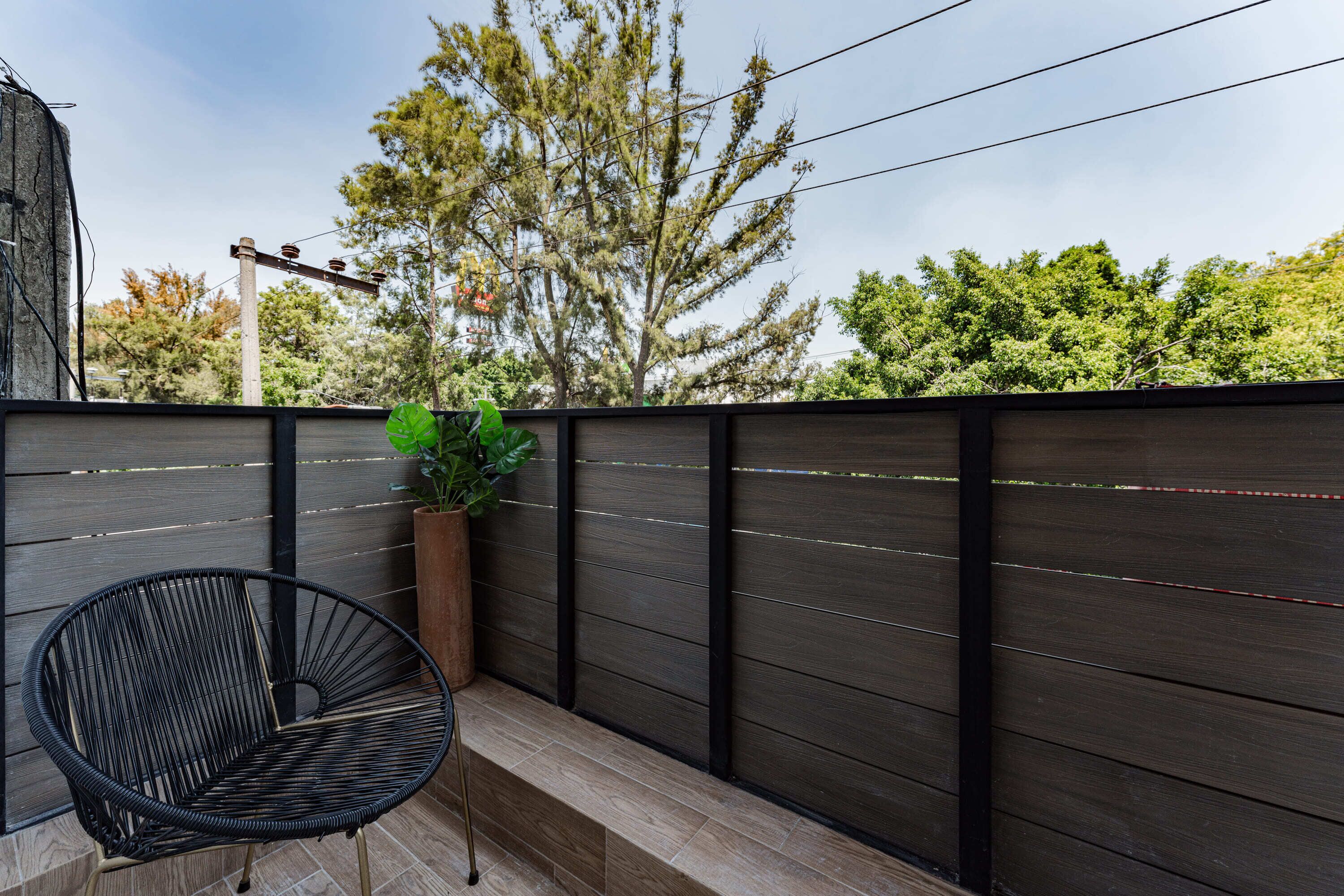 A balcony with a dark wooden fence, a wicker chair, and a potted plant.