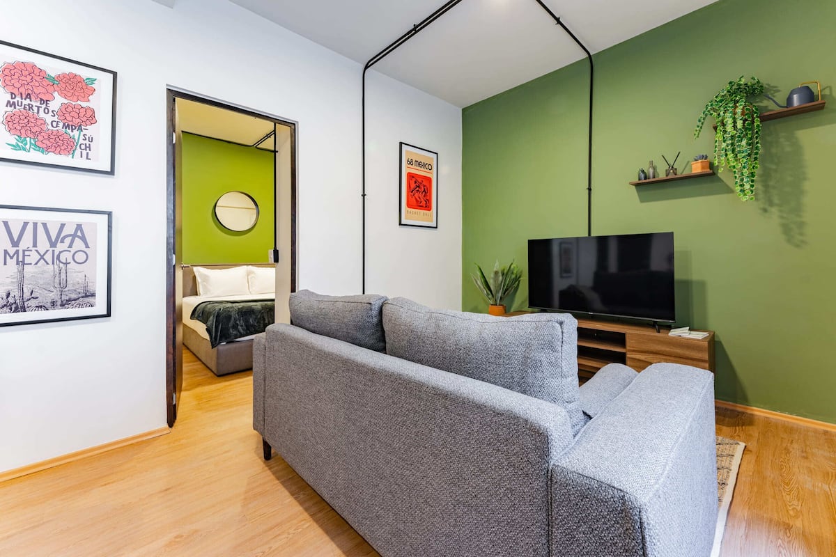 Una sala de estar moderna con un sofá gris, un televisor de pantalla plana y paredes verdes.