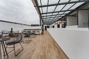 Une terrasse moderne sur le toit, dotée d’un plancher en bois, de chaises en métal noir et de plantes en pot.