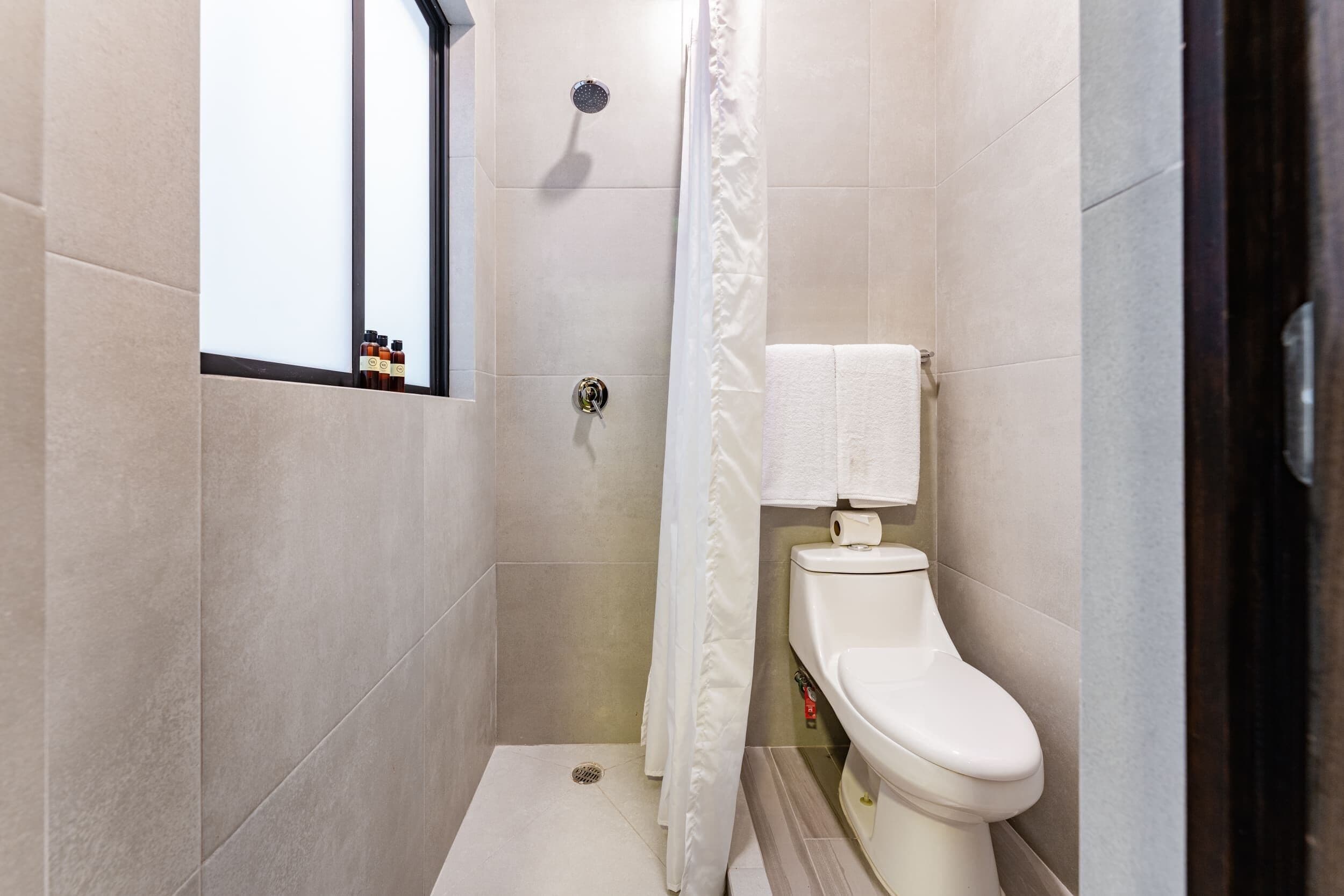 Een compacte, moderne badkamer met een douche, toilet en een raam.