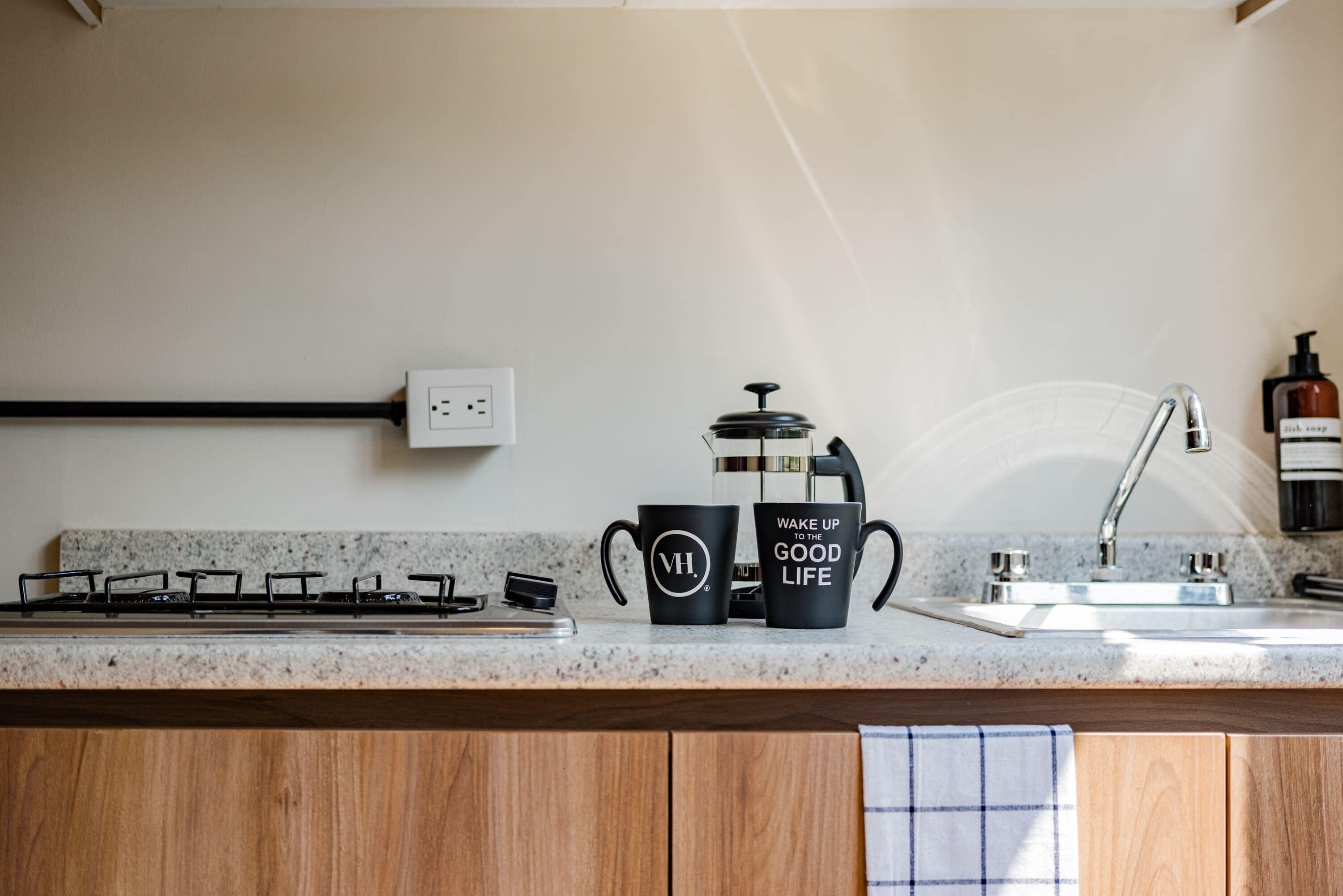 A kitchen with a gas stove, a coffee maker, and two black mugs on the countertop.