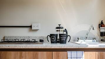 A kitchen with a gas stove, a coffee maker, and two black mugs on the countertop.